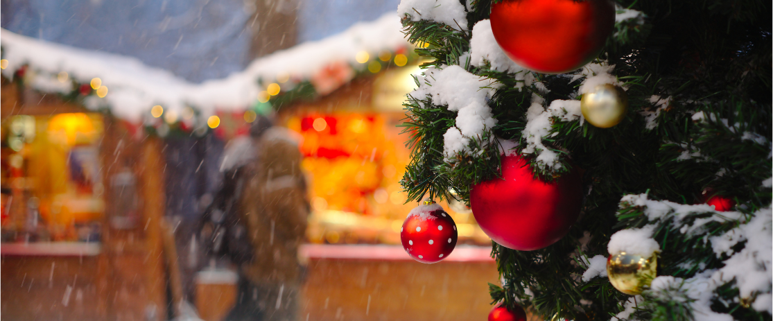 Verschneite Weihnachtsmarktbuden mit zwei Besuchern in winterlicher Atmosphäre.