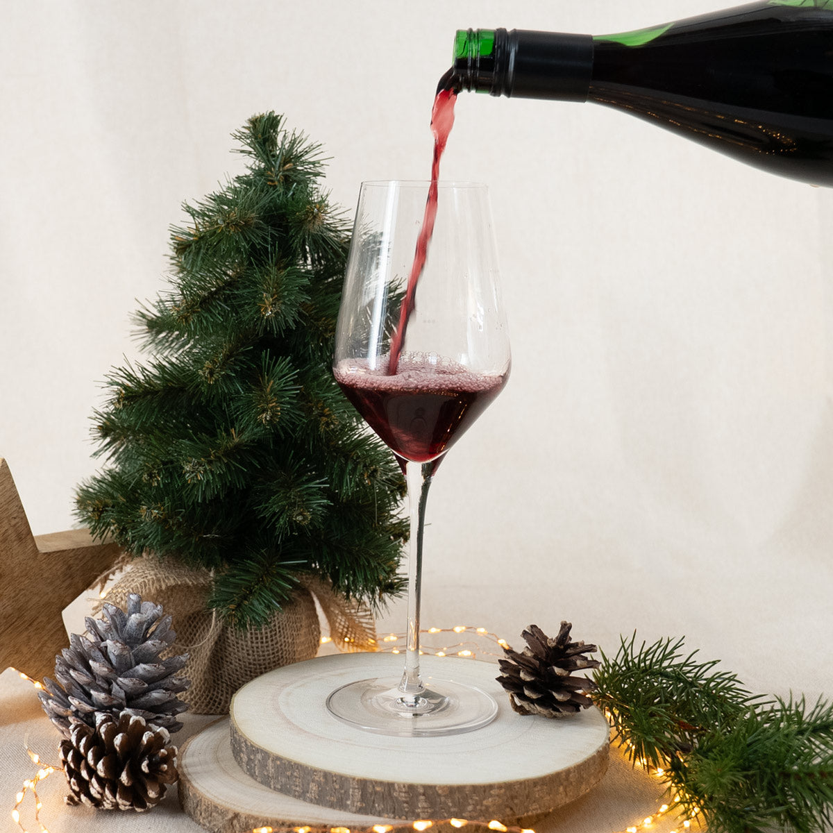 Glas wird mit rotem Glühwein befüllt und steht auf einer Holzplatte mit weihnachtlicher Dekoration