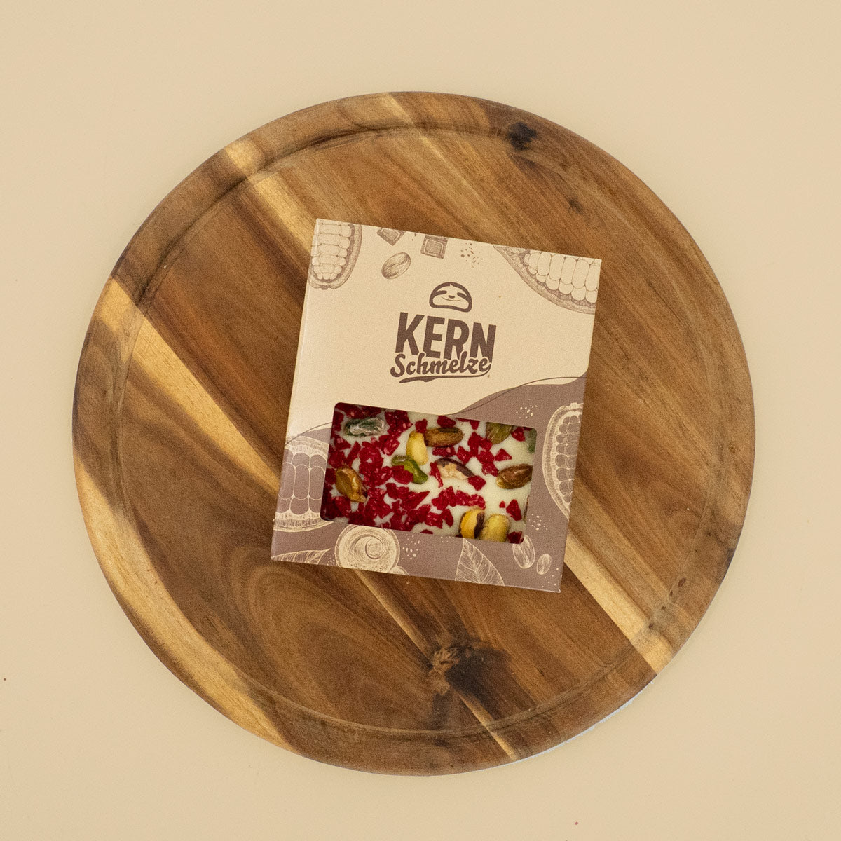 Schokoladentafel mit weißer Schokolade, Pistazien und Himbeeren in Standardverpackung auf Holztablett