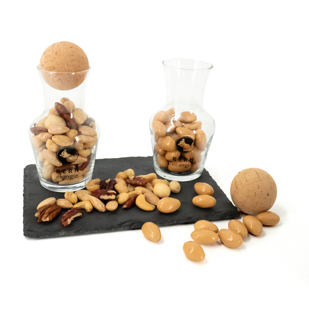 Zwei befüllte Glas-Dekanter auf einer dunklen Steinplatte mit Nüssen von KERNenergie.