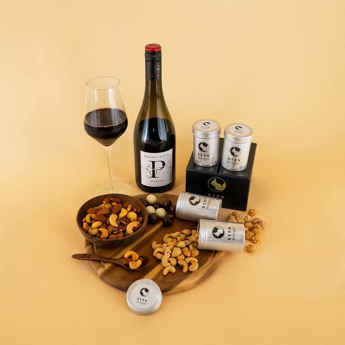 Rotwein und Geschenkset mit vier Aludosen und verschiedenen Nüssen auf Holztablett