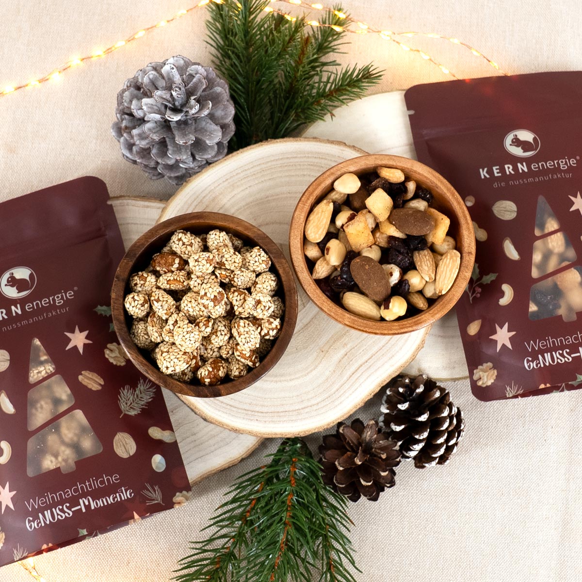 Gebrannte Erdnüsse und eine Nussmischung in Holzschalen mit weihnachtlichen Snackbeuteln daneben