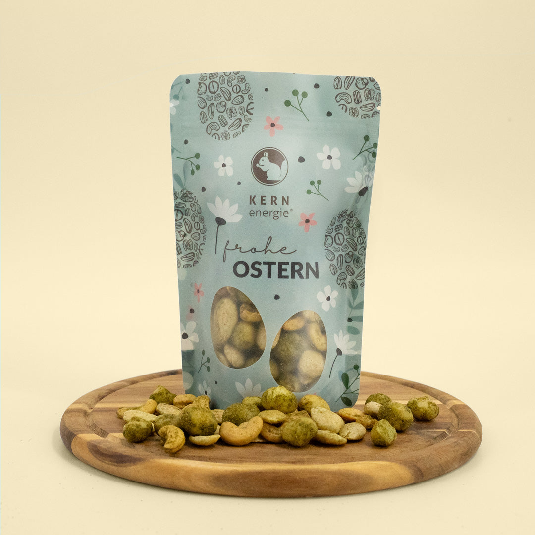 Blauer Snack Beutel mit Osterdruck gefüllt mit Nussmischung mit Bärlauch Gewürz auf Holzteller verteilt