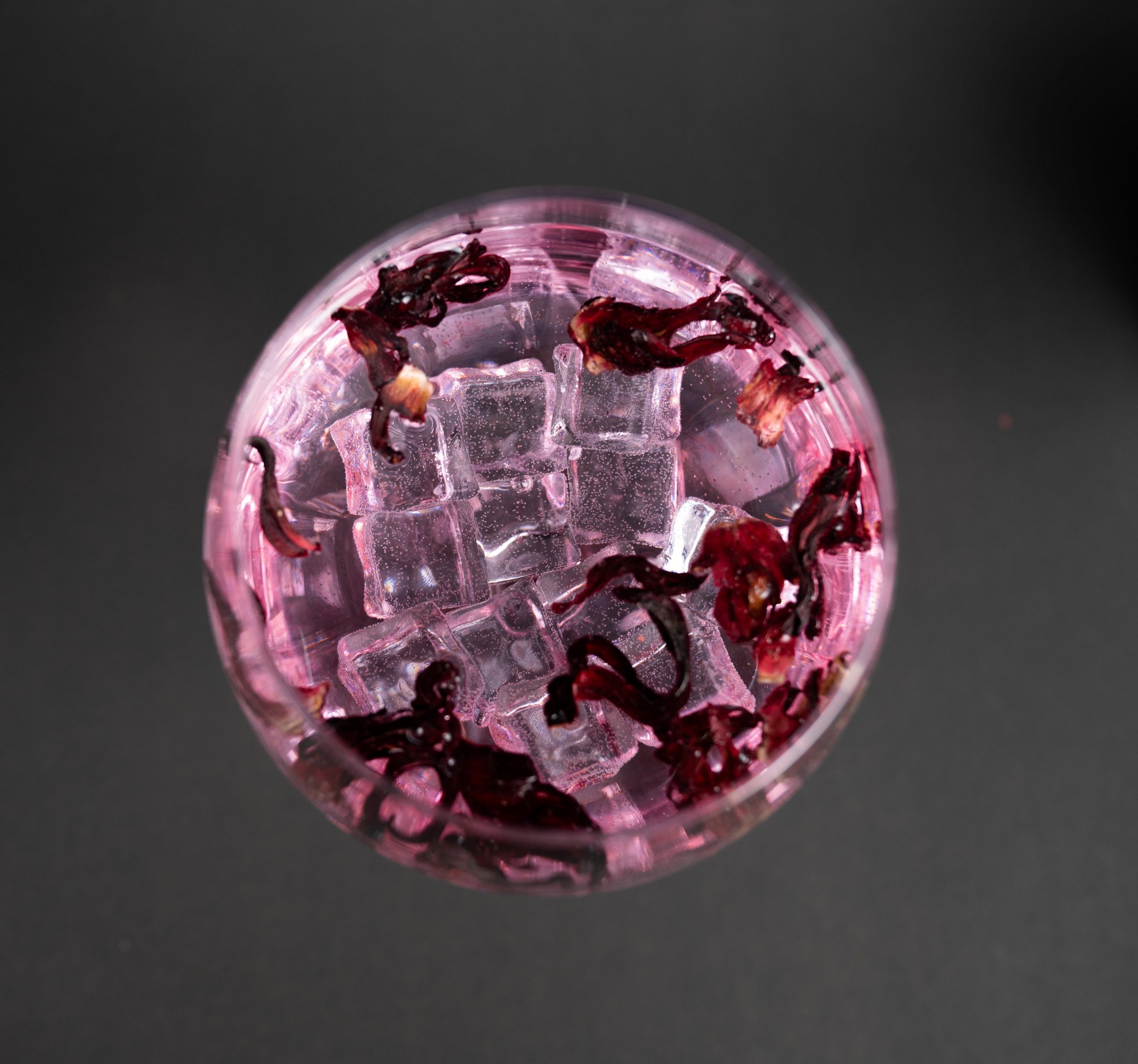 Gin Glas vor schwarzem Hintergrund gefüllt mit leckerem Gin, Eis und Rosa Blüten