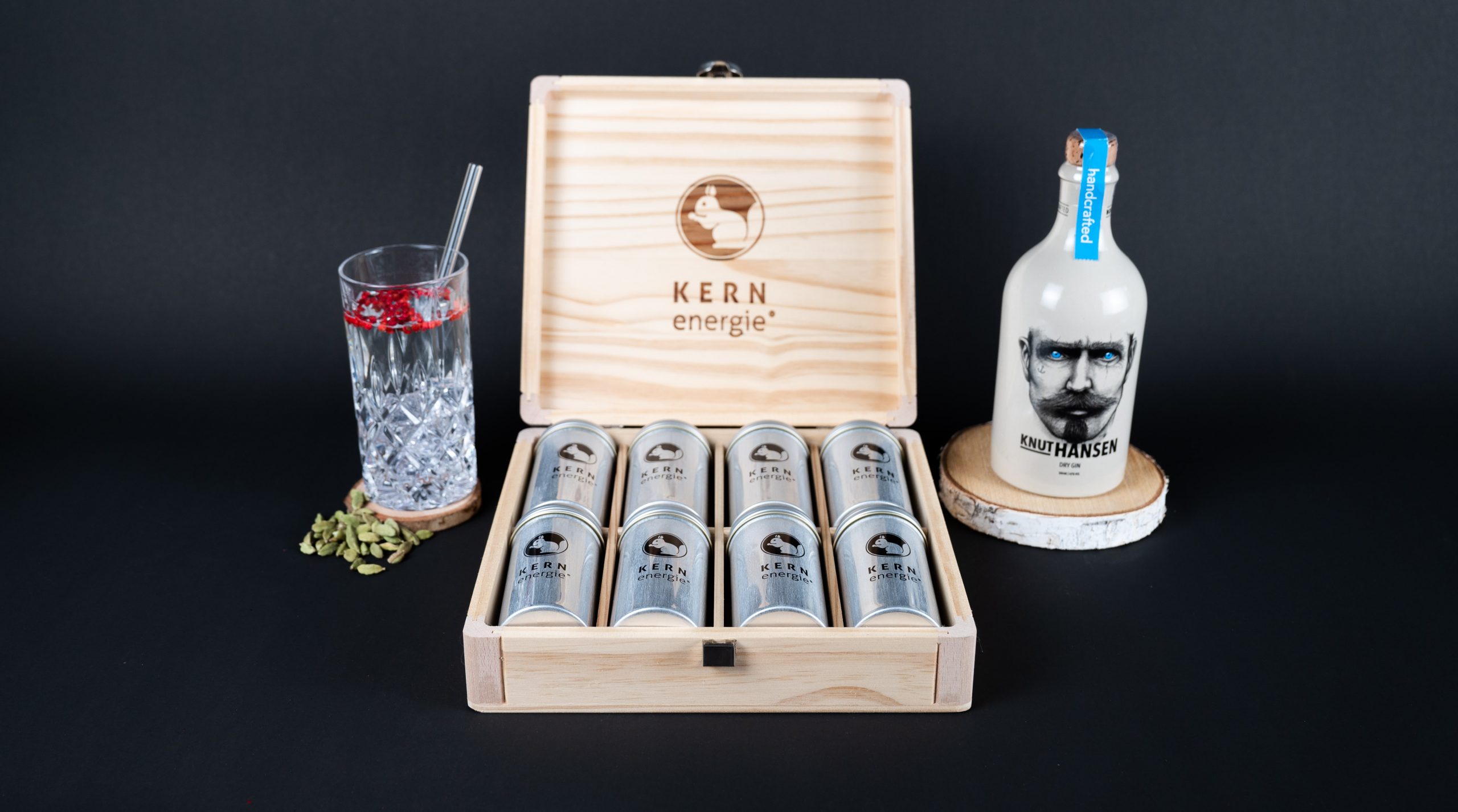 Das KERNenergie Zutaten Set in der edlen Holzbox zwischen einem Cocktail Glas und einer Flasche Knut Hansen vor schwarzem Hintergrund