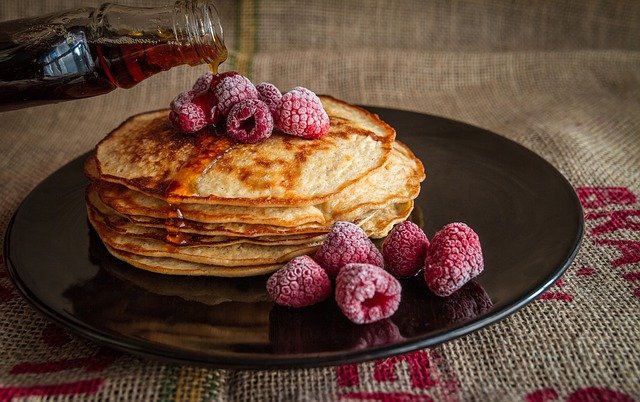 Pancakes auf Teller mit Ahornsirup und Himbeeren